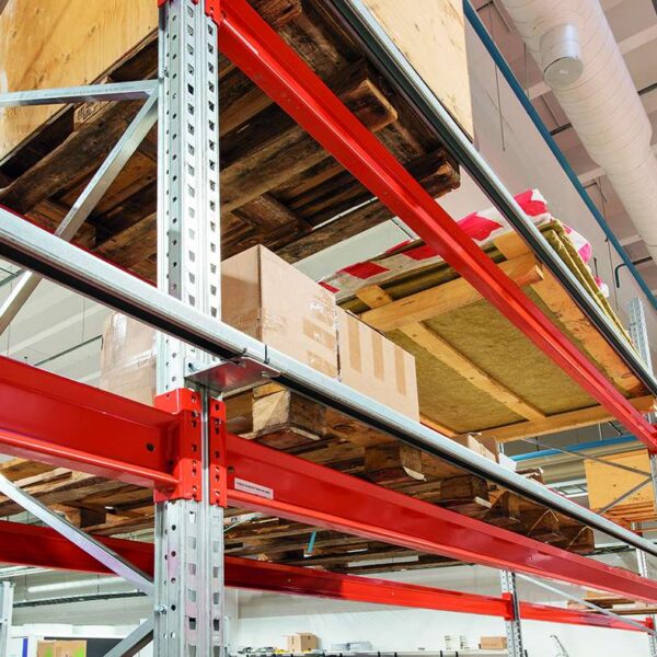 Industrial warehouse storage rack with wooden pallets and cardboard boxes on metal shelving, red supports overhead